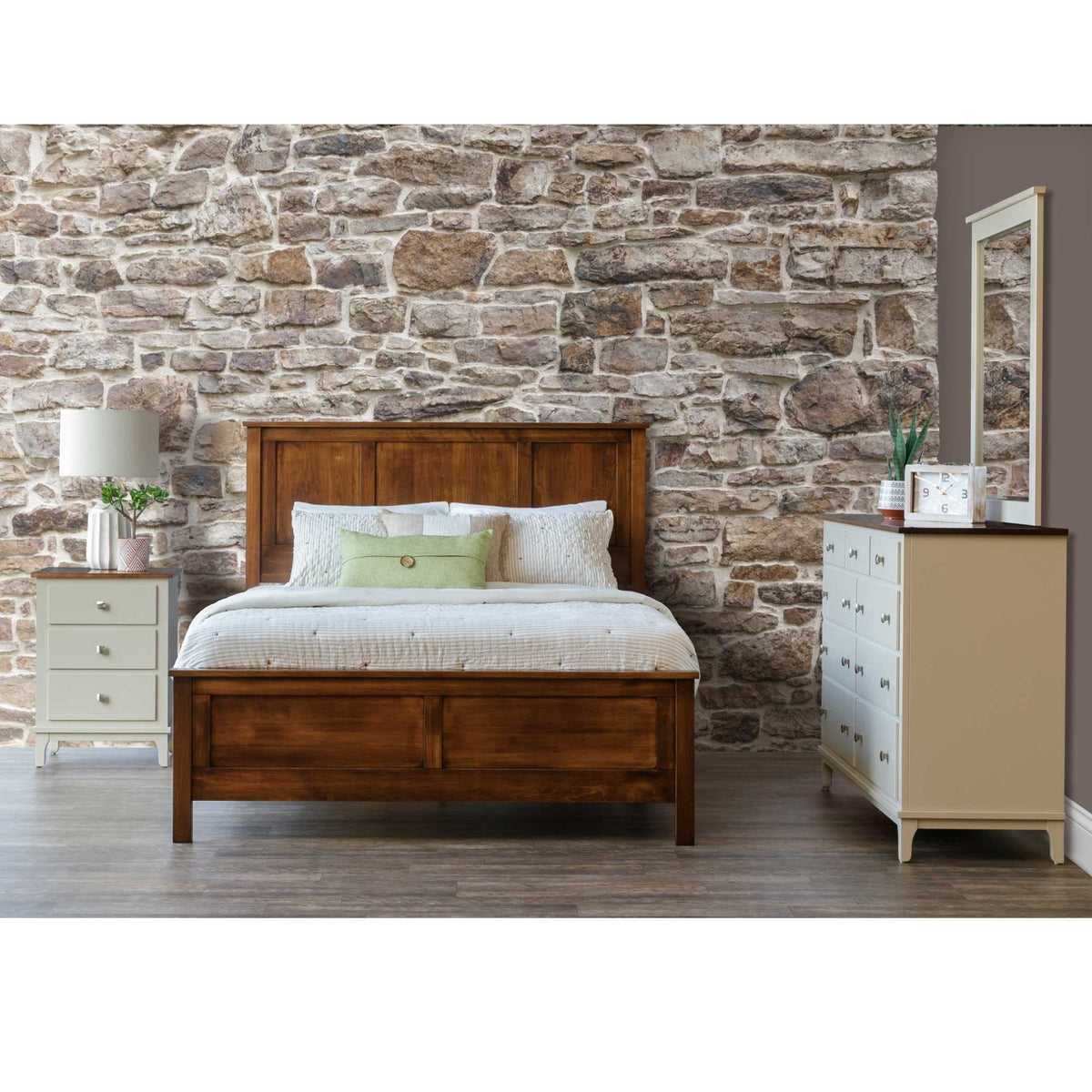 Four-piece panel bedroom set with a warm brown wood bed, cream painted nightstand and mirrored dresser against a fieldstone wall