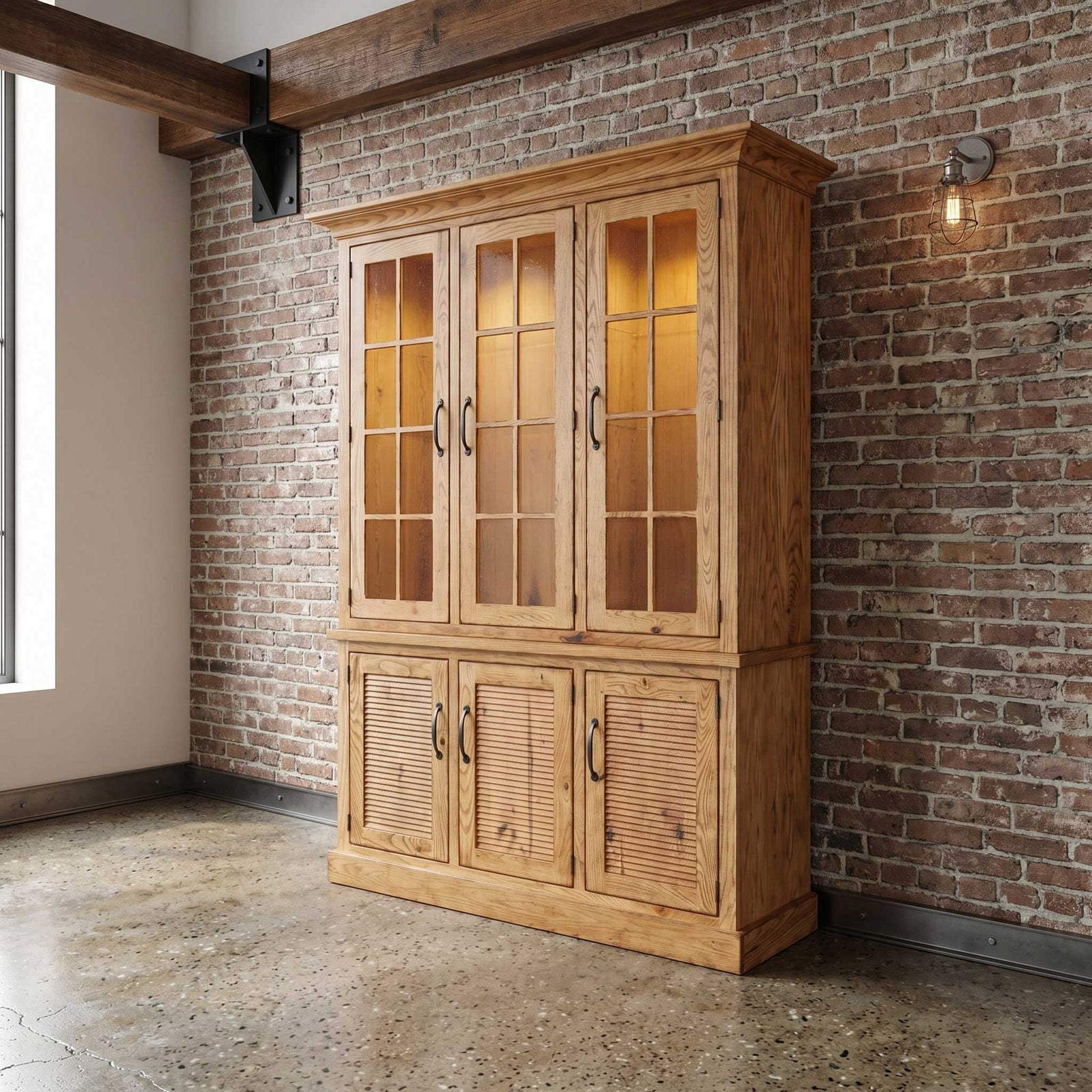 Natural oak three-door china cabinet with lit nine-pane glass doors over louvered base doors in a brick loft