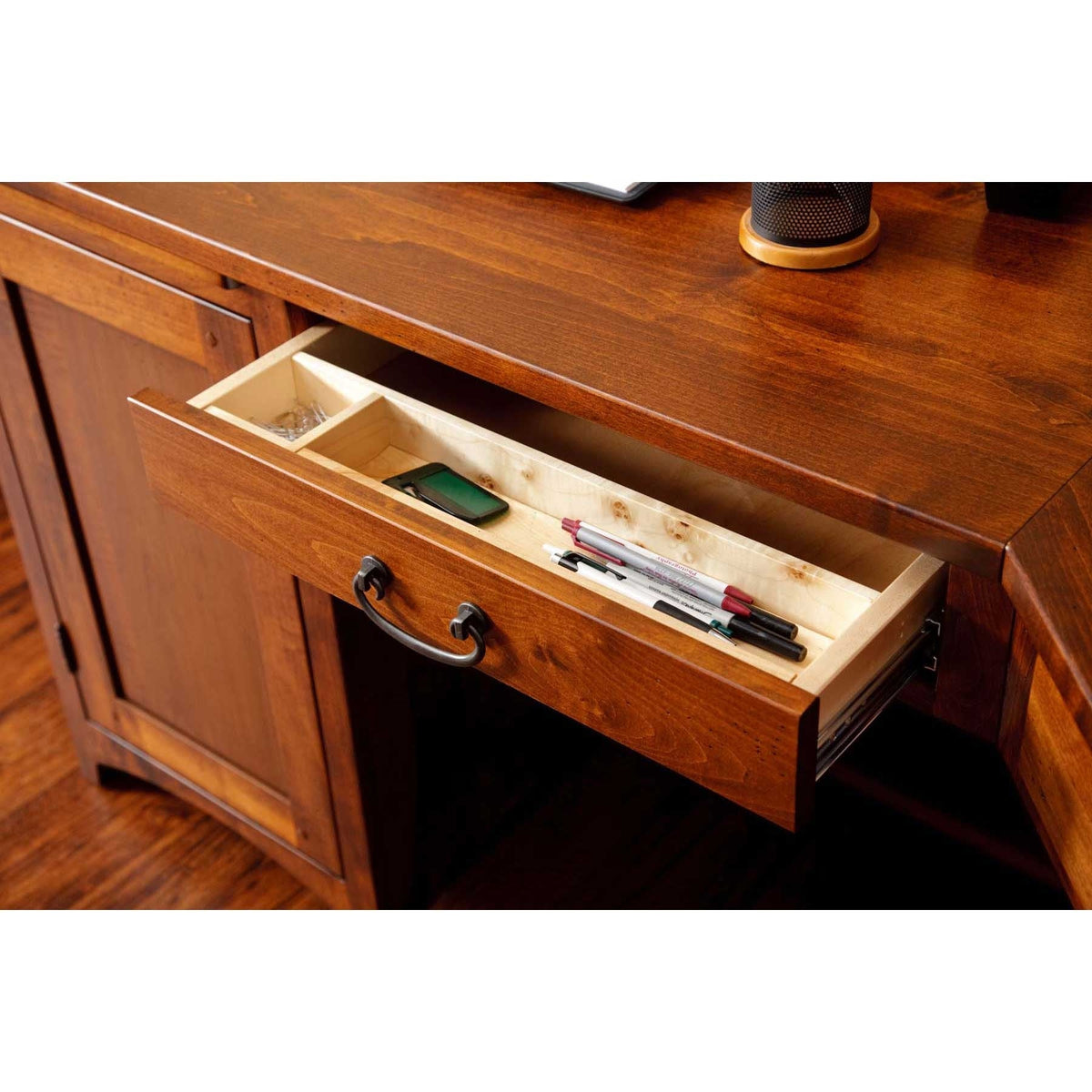 Cherry desk with a top drawer pulled open showing the light maple divided interior with pens and a phone