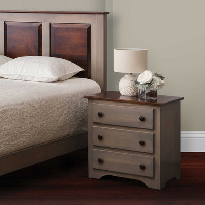 Gray stained three-drawer nightstand with a contrasting dark walnut top beside a paneled bed and lamp