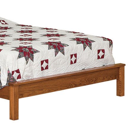 Close-up of the oak bed's footboard and solid side rail with a quilt draped over the mattress edge