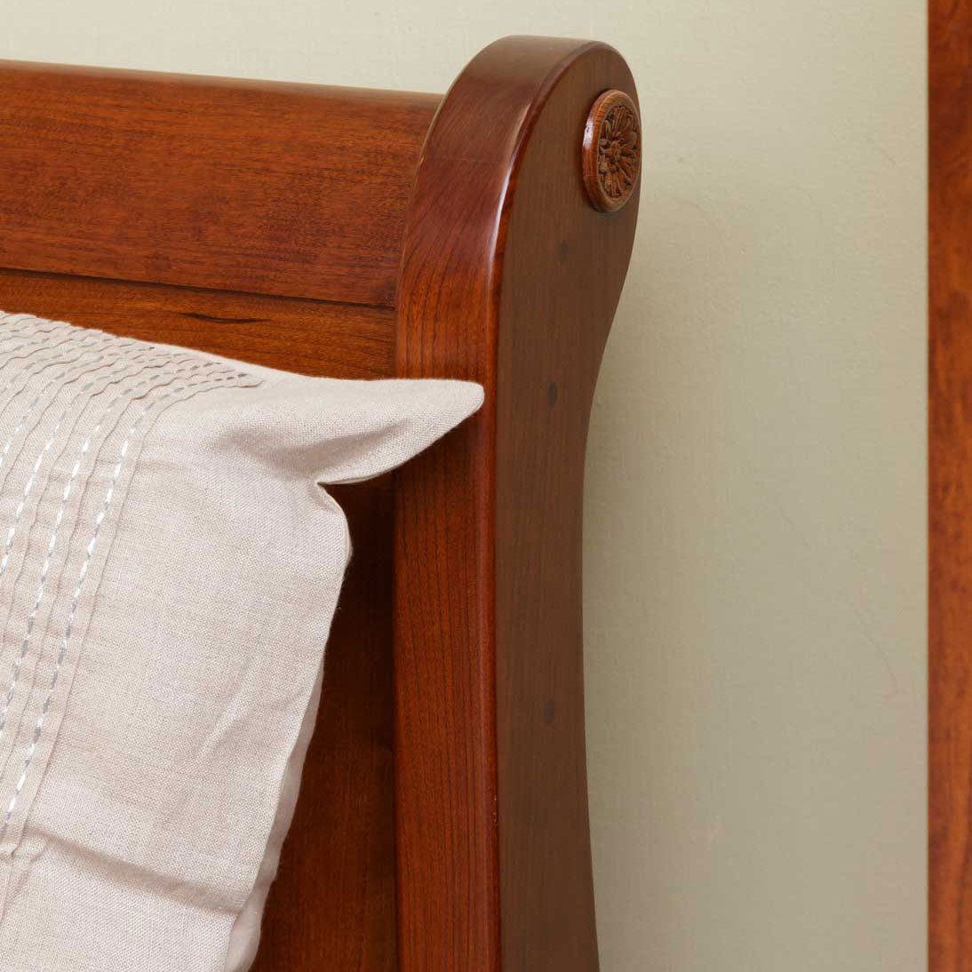 Curved cherry sleigh headboard end with carved rosette, seen behind stitched neutral pillows