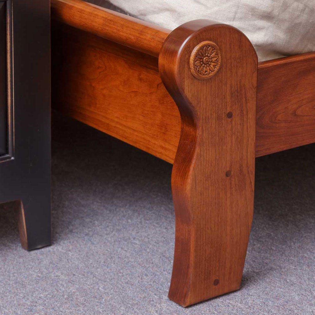 Shaped cherry footboard end of the sleigh bed with a rosette medallion and exposed wood pegs