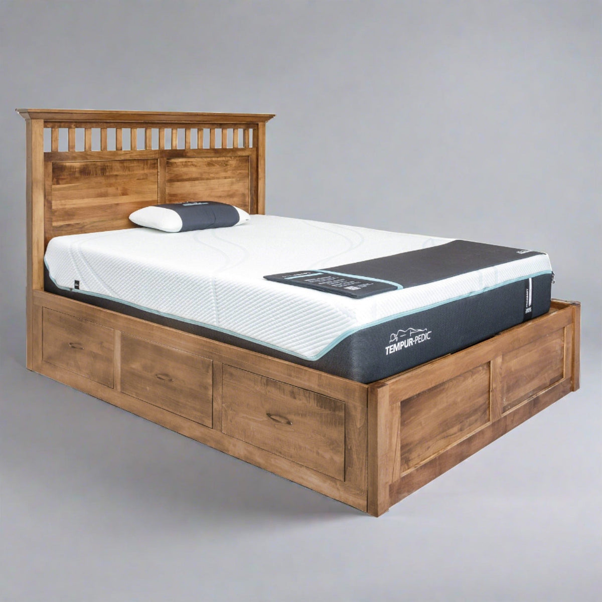 Rustic wood platform storage bed with slat and panel headboard, three base drawers and a mattress, gray backdrop