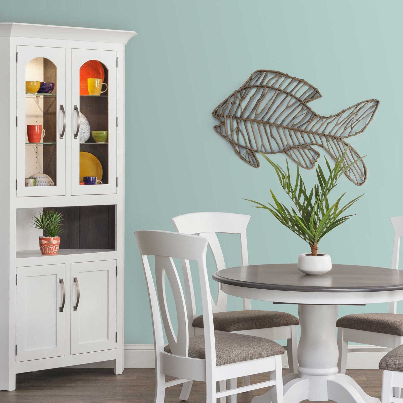 White painted corner china cabinet with arched glass doors, colorful dishes on lit shelves and a two-door base
