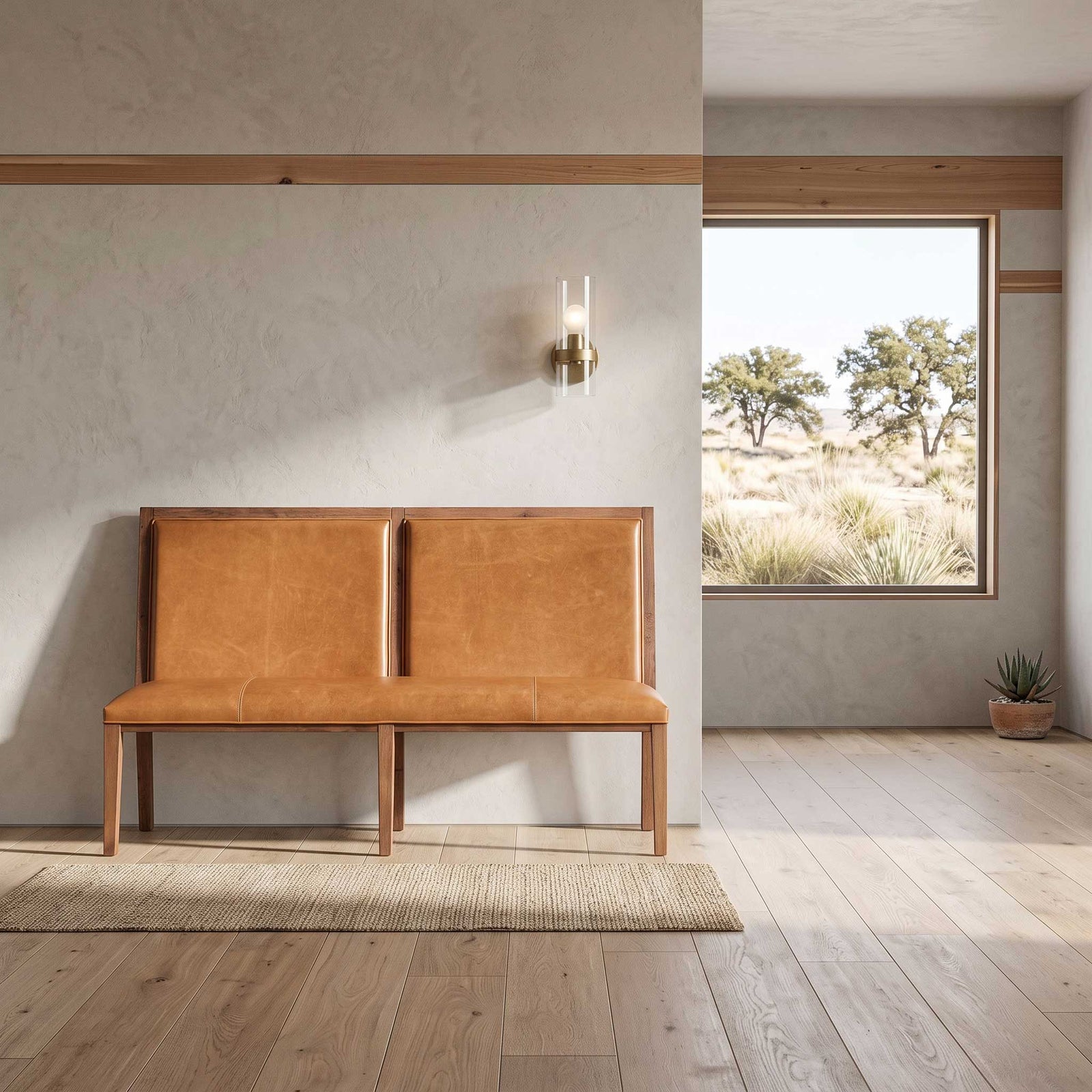 A mid-century modern two-seater bench with tan leather upholstery and a light wood frame, placed on a woven rug in a minimalist room with a window showing an outdoor landscape.