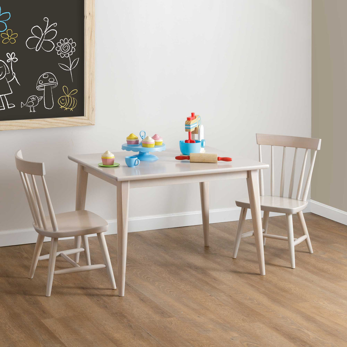 Toddler table and two spindle back chairs in a pale finish arranged with a toy tea party and chalkboard art