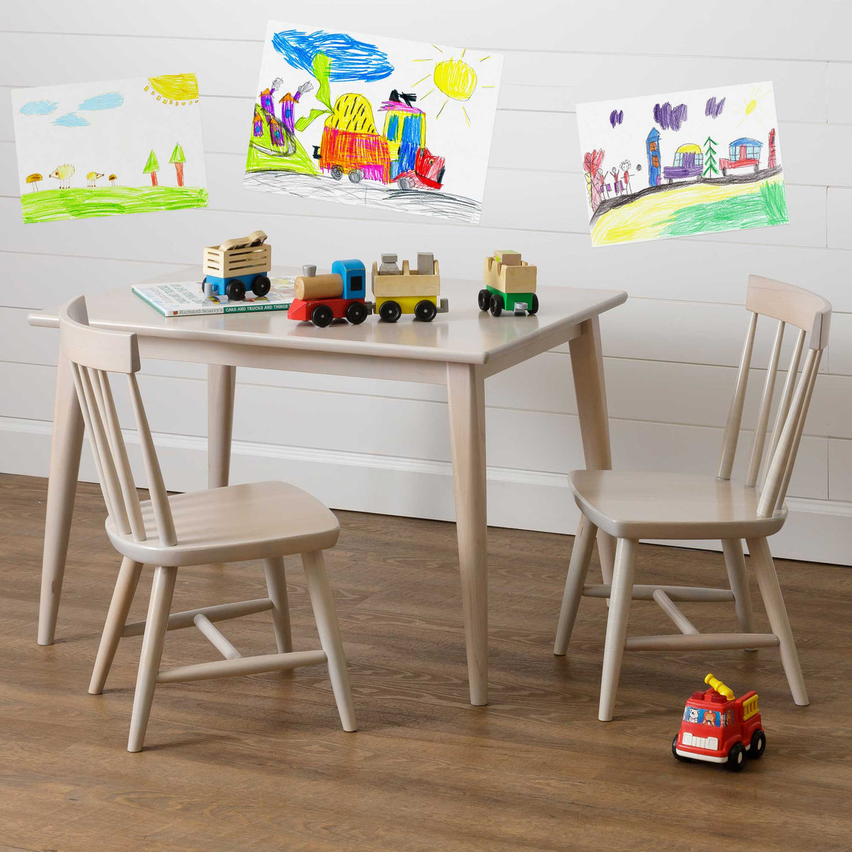 Children's play table and chair set in whitewashed wood with toy trains and a fire truck on the floor