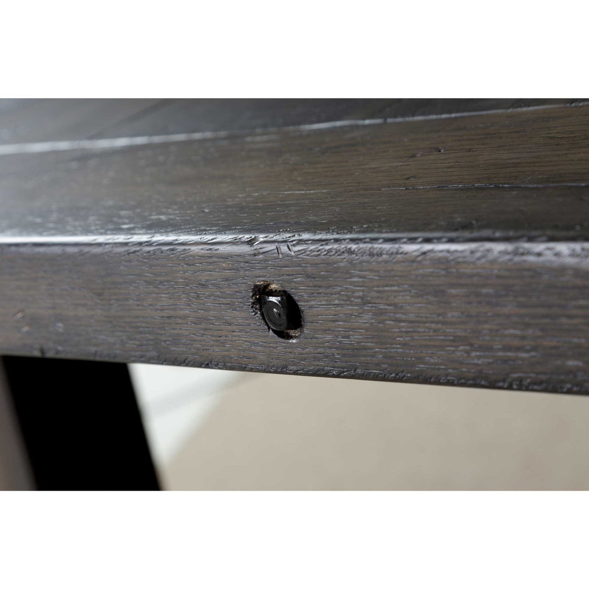 Close view of a black bolt head recessed into the table apron of the gray trestle base