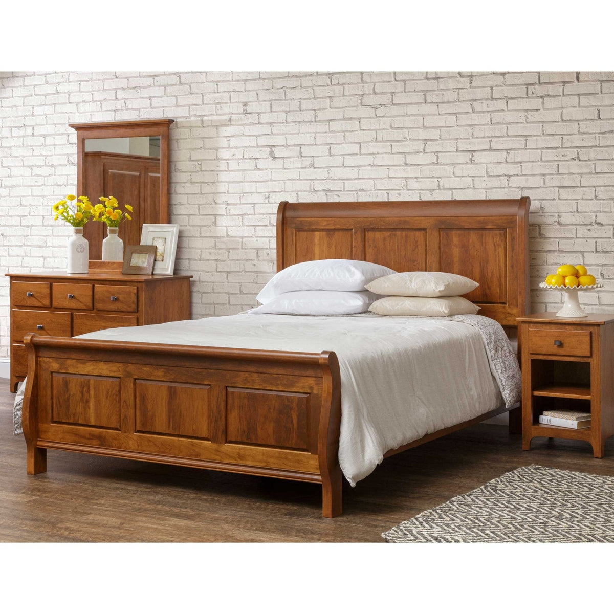 Cherry sleigh bed with raised panel headboard and footboard, styled with white bedding beside a dresser and nightstand