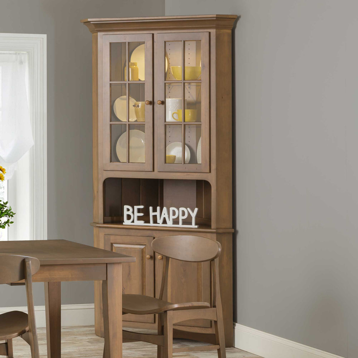 Light stained corner china cabinet with lit mullioned glass doors, yellow dishware and a paneled two-door base