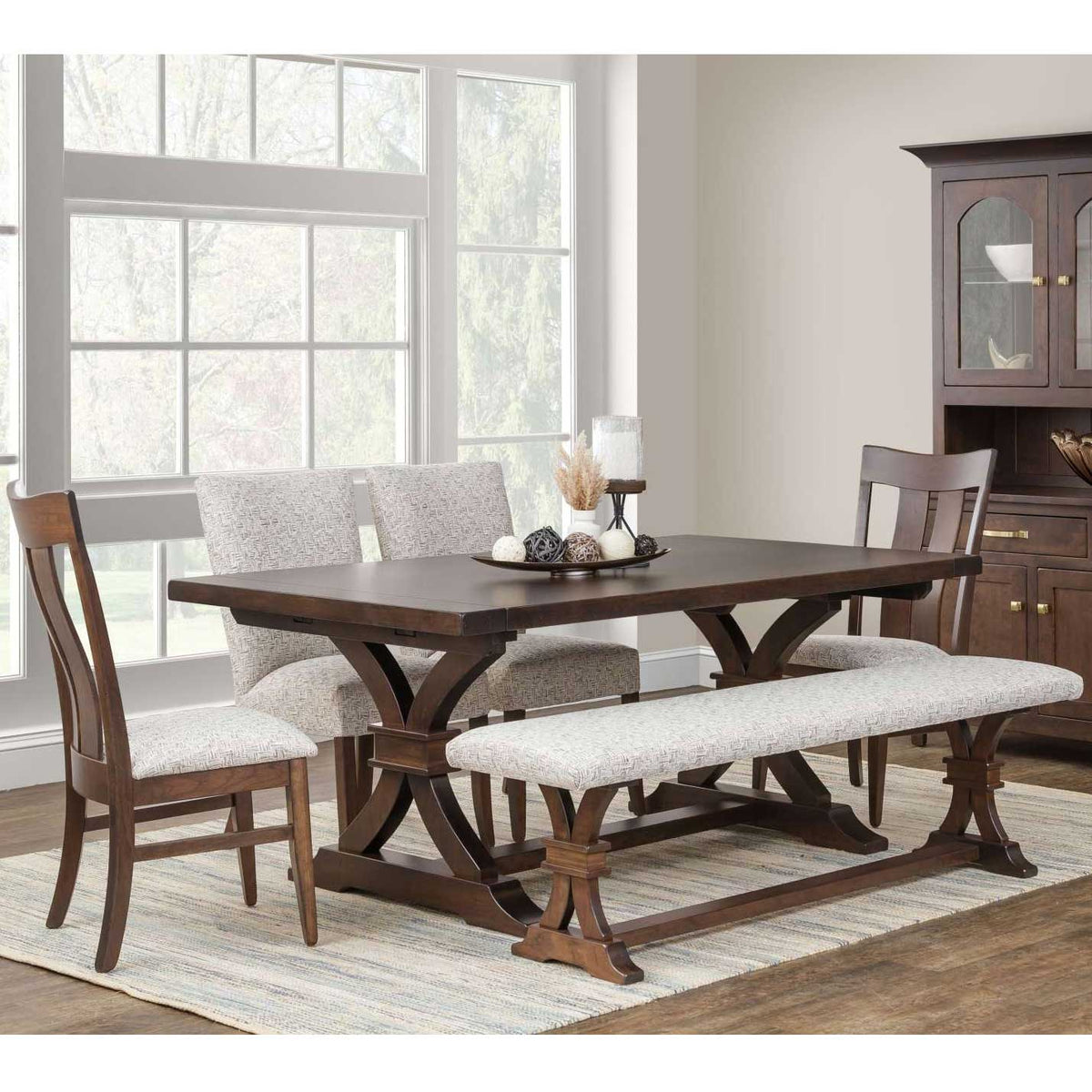 Sherwood trestle table with dark plank top and curved trestle base, styled with upholstered chairs, bench and china cabinet