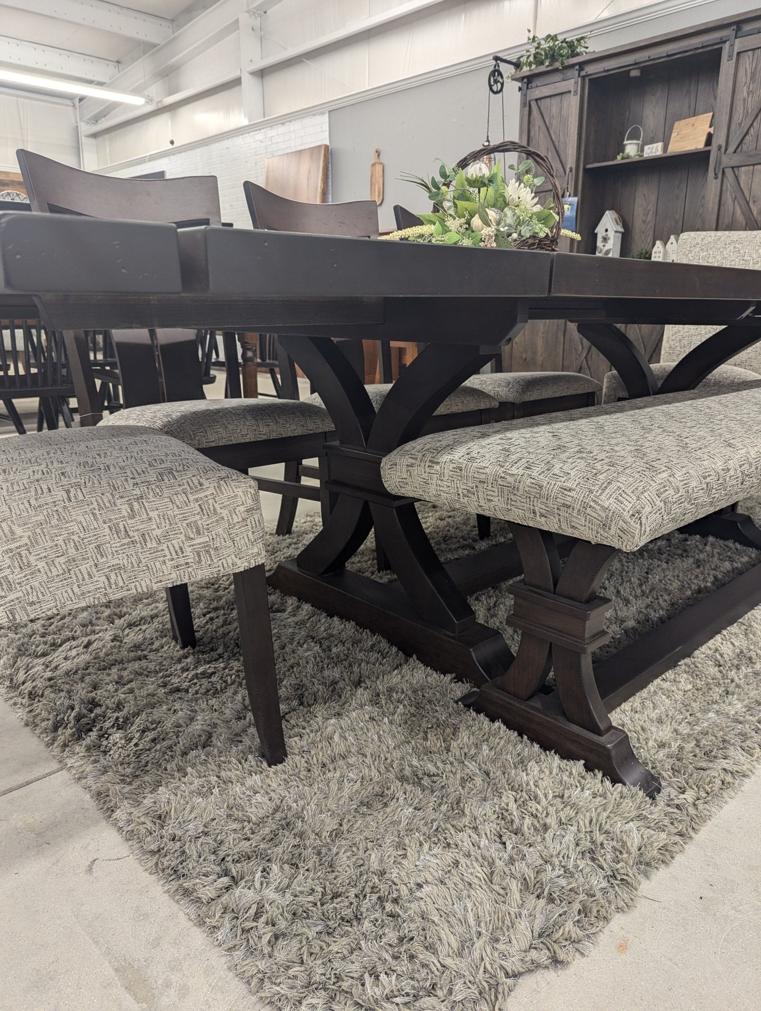 Dark brown trestle dining table with two panel back chairs, two upholstered side chairs and a matching bench, on white