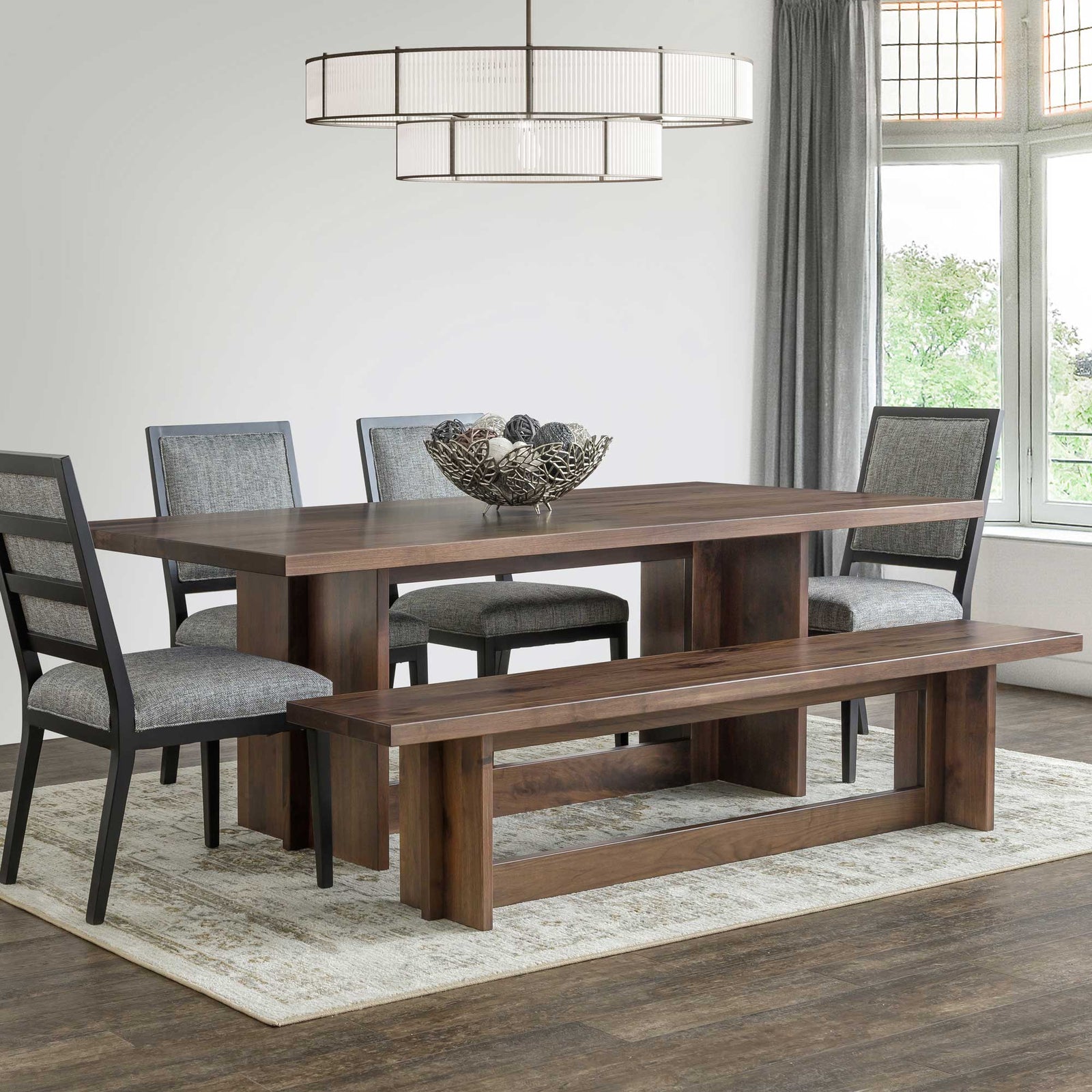 Walnut Sophia trestle table with panel base under a drum chandelier, gray upholstered chairs and plank bench