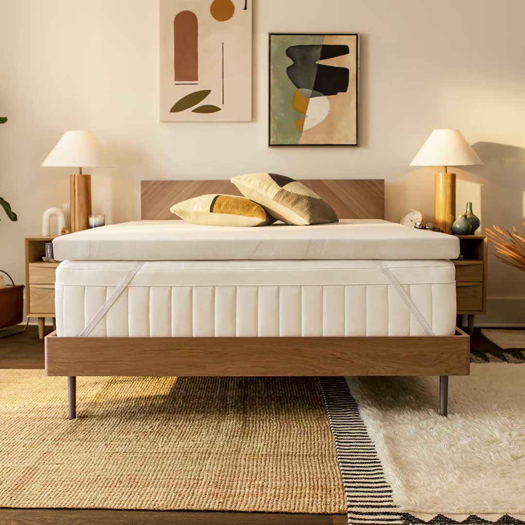 Mattress topper on a bed in a warm neutral bedroom with wood headboard, matching lamps and layered rugs