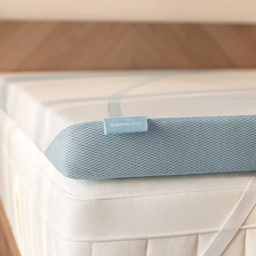 Close-up of the topper's elastic anchor strap and label wrapping over the corner of a white mattress