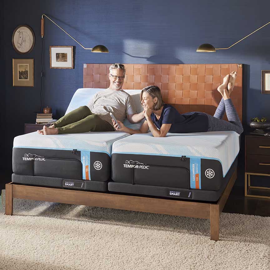 Couple relaxing on a split king with heads raised on adjustable smart bases in a navy bedroom with leather headboard