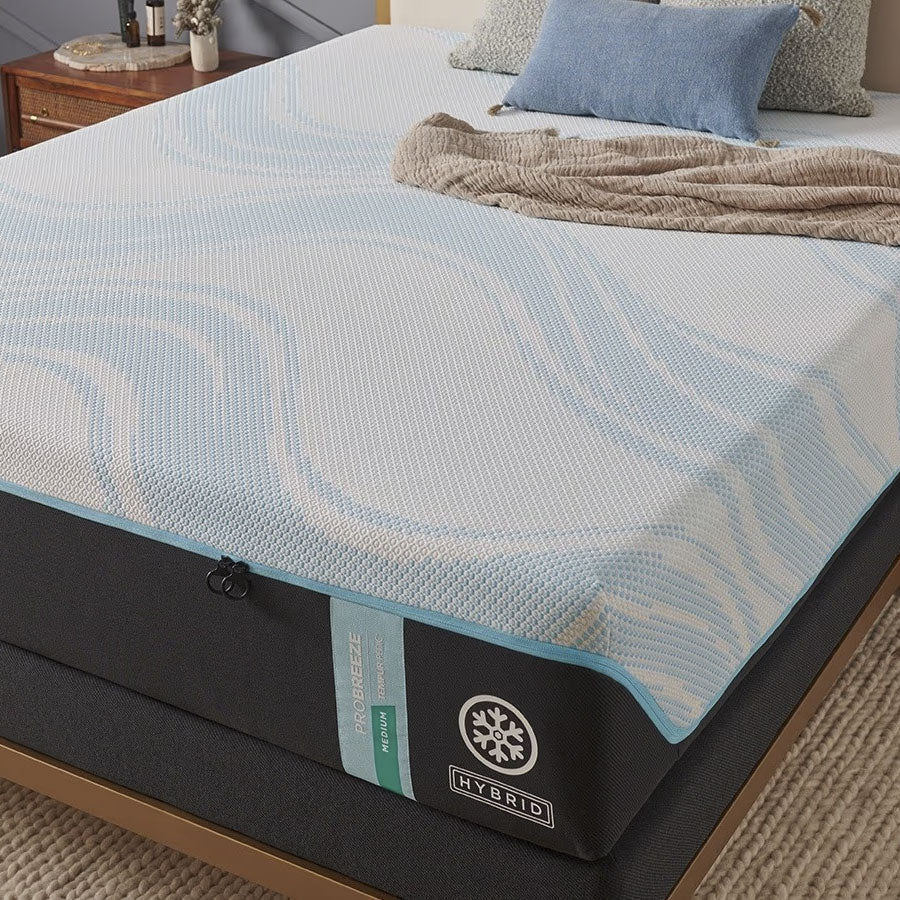 Corner of a medium cooling hybrid mattress on a gold bed frame, styled with a blue pillow and knit throw