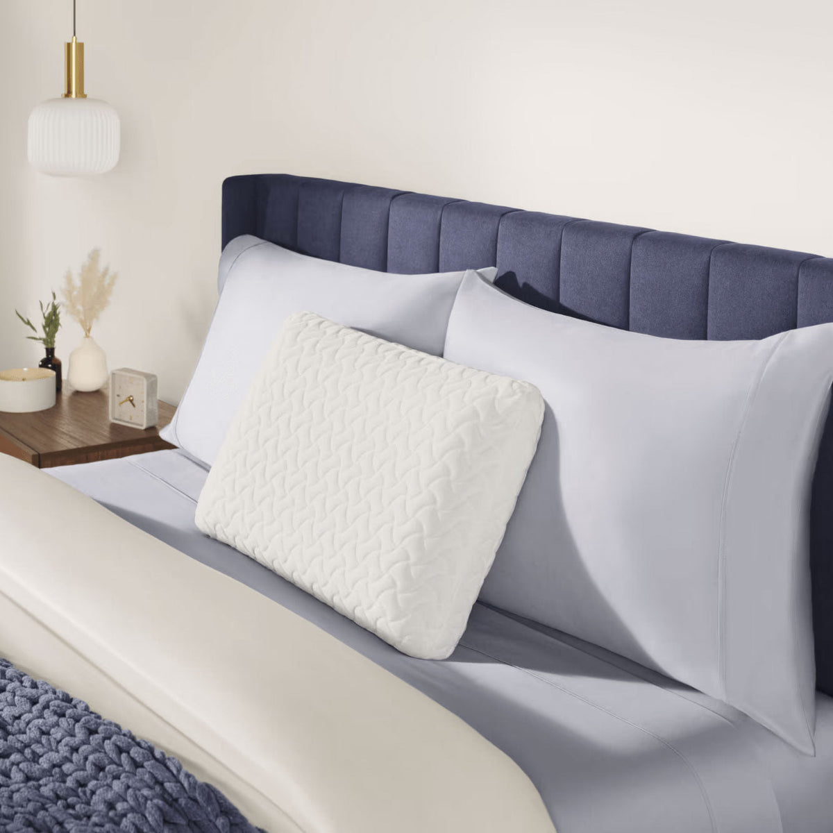 Quilted white bed pillow propped against gray pillows on a navy channel-tufted headboard bed