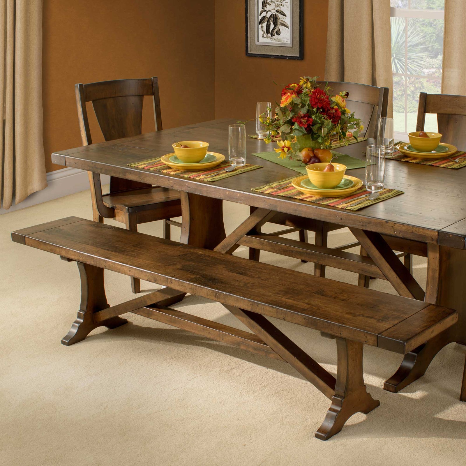 Westin trestle dining bench in warm brown maple beside a matching trestle table set with yellow dishes and flowers