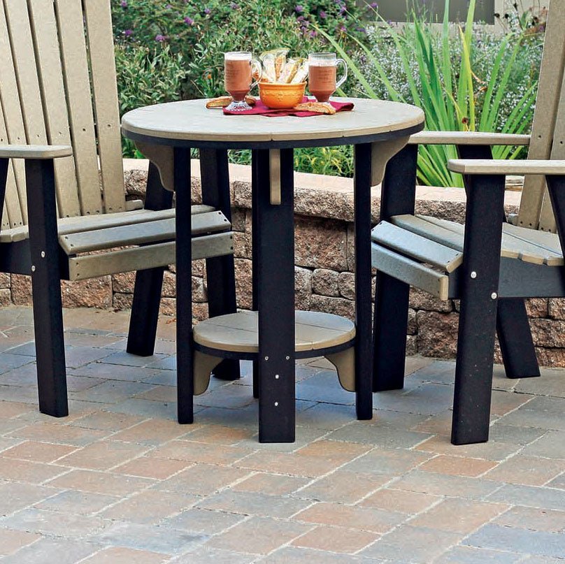 Weathered wood and black poly bistro patio table with a round top and lower shelf between two chairs on a paver patio