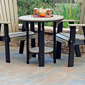 Weathered wood and black poly bistro patio table with a round top and lower shelf between two chairs on a paver patio