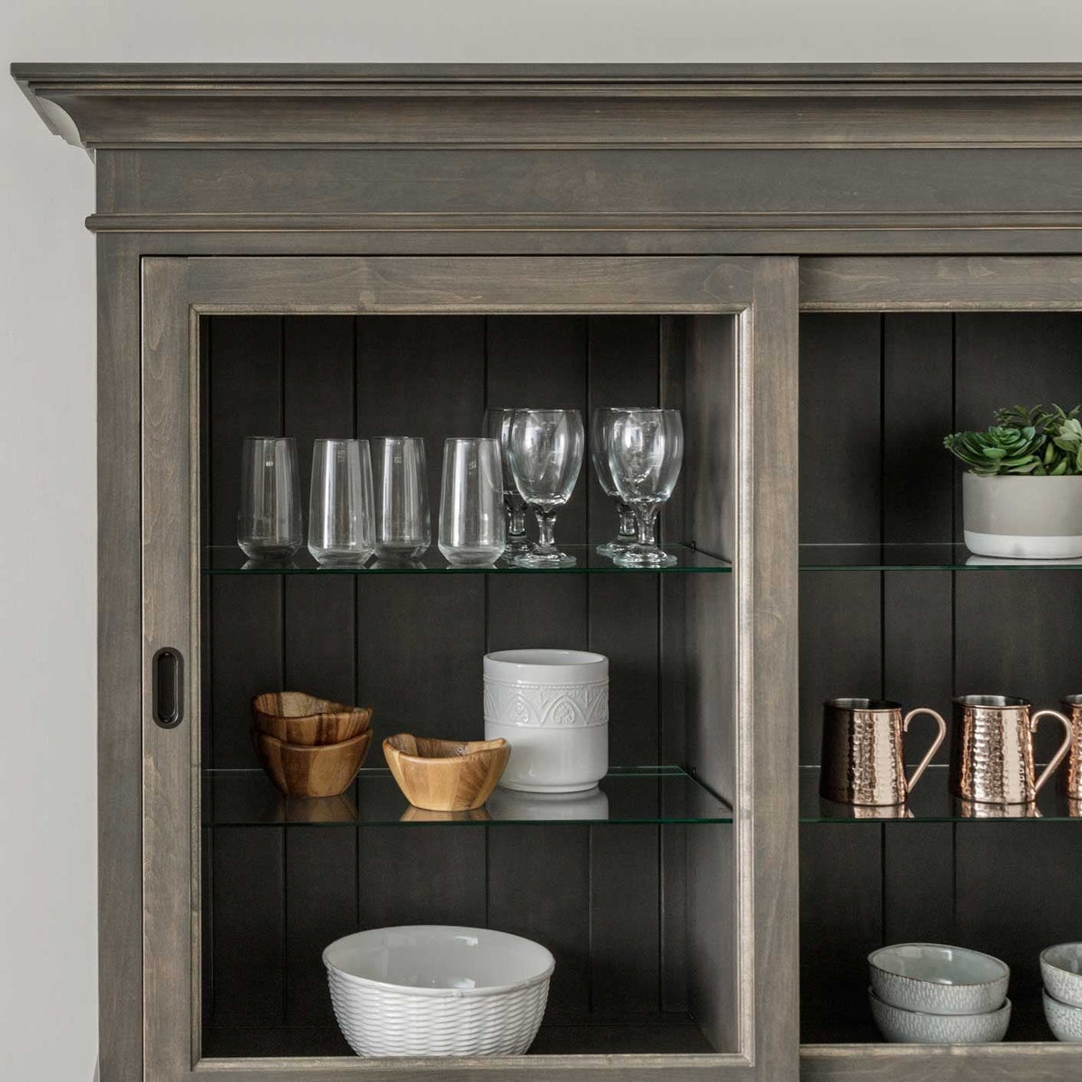 Detail of a gray china cabinet interior with glass shelves, dark plank back and displayed glassware and bowls