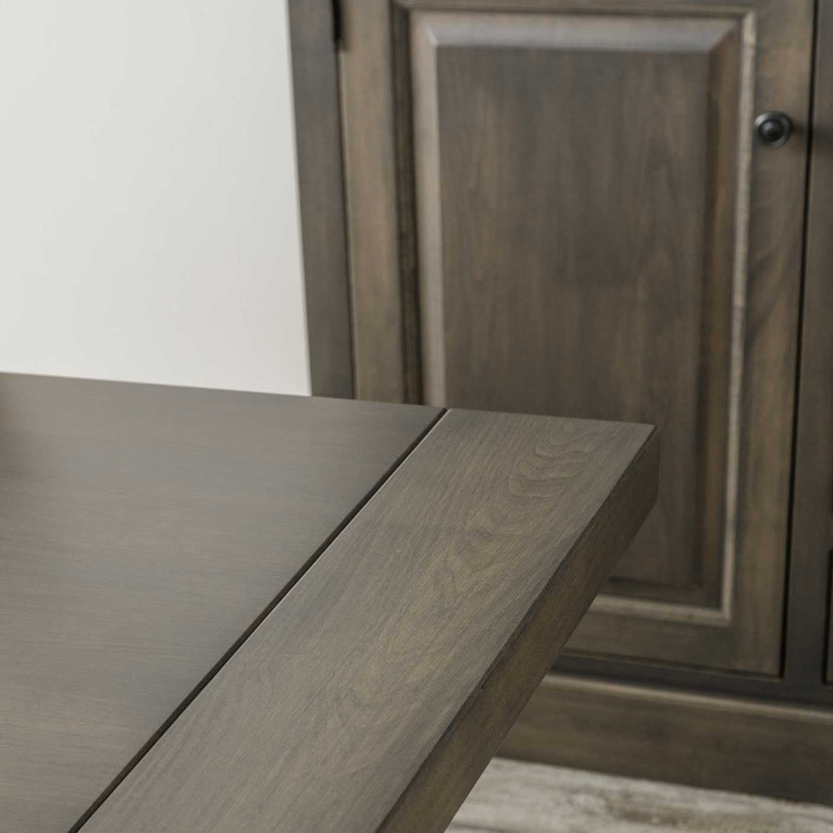 Close view of the gray dining table edge and self storing leaf seam in front of a matching cabinet door