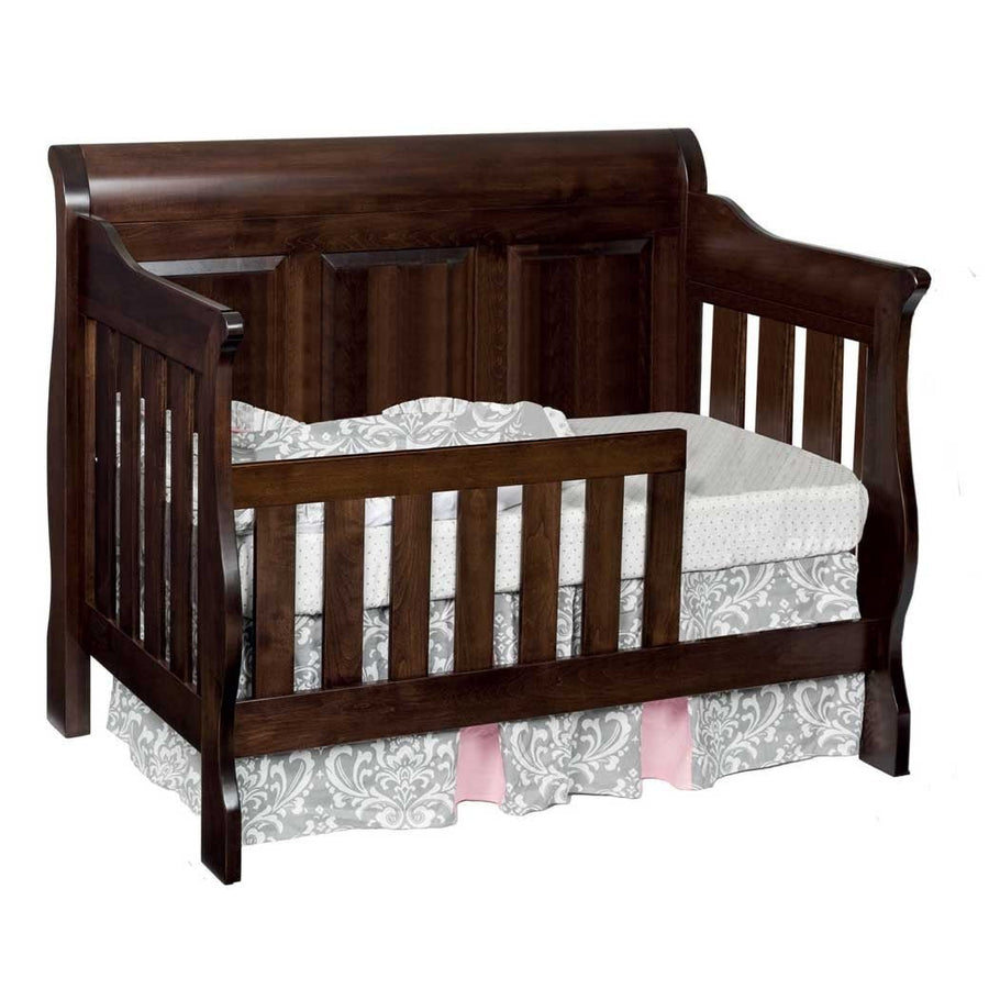 Dark espresso convertible crib set up as a toddler bed with a slatted safety rail and gray bed skirt