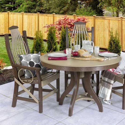 Round poly dining table set for a meal with two high back chairs on a concrete patio by a wood fence