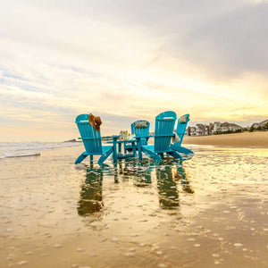 Three aqua blue poly Adirondack chairs with a side table on wet sand at sunset by the shoreline