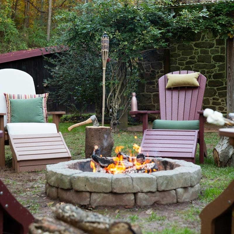 Cedar and cranberry poly Adirondack chairs with cushions and an ottoman around a stone fire pit