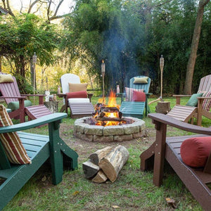 Circle of green, red and cedar poly Adirondack chairs with pillows around a blazing backyard fire pit