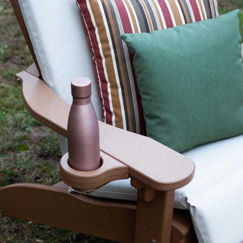 Cedar toned Adirondack chair arm with an inset cup holder holding a bottle beside striped pillows