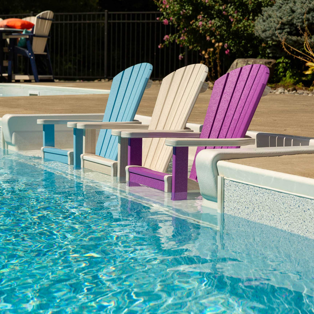 Row of blue, tan and purple poly Adirondack chairs lined along the edge of a backyard swimming pool