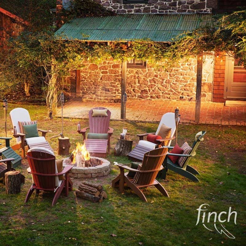 Evening fire pit gathering with cushioned poly Adirondack chairs and ottomans by a stone farmhouse