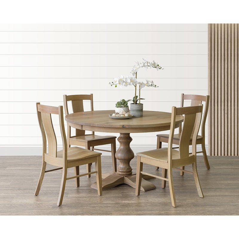 Light oak round pedestal table set with four dining chairs and a white orchid centerpiece in a bright shiplap room