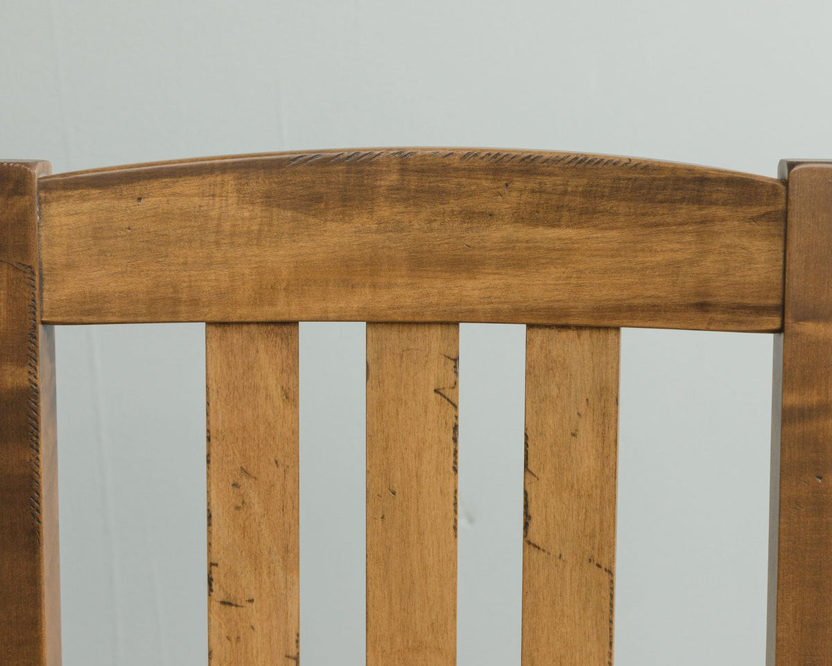 Detail of the curved top rail and slats of a rustic maple bar chair against a pale gray wall