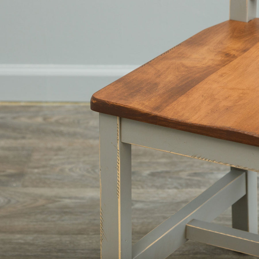 Close view of a gray painted chair leg and stretcher with a warm brown scooped wood seat above