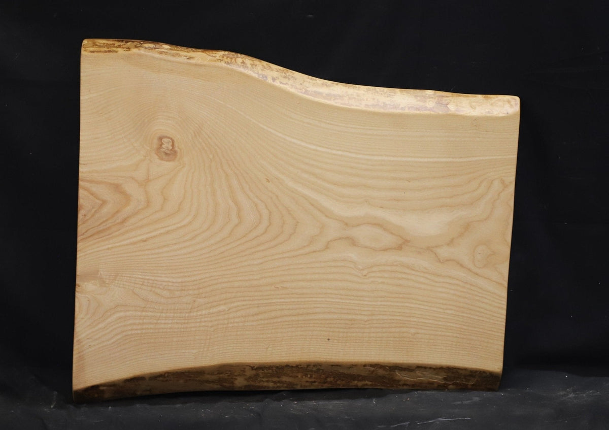 Small ash live edge slab with bark along one edge, gently wavy sides and quiet straight grain on black