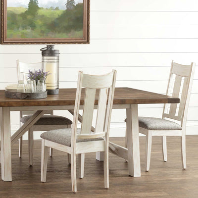 Whitewashed dining chairs with gray fabric seats around a trestle table with a natural brown plank top