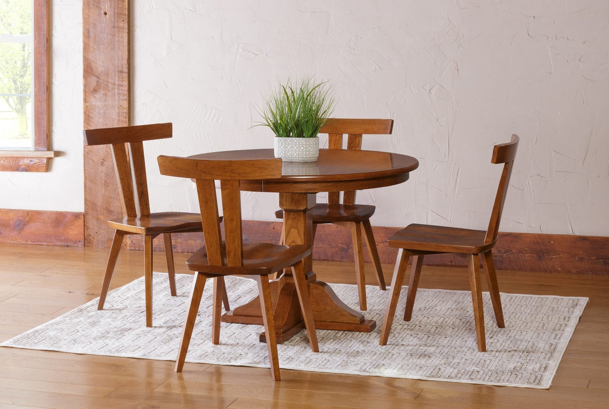 Round cherry pedestal table with four Astoria T-back dining chairs on a patterned rug in a sunlit room