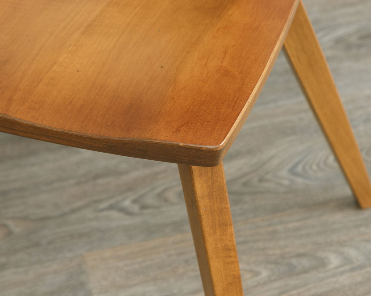 Detail of the sculpted saddle seat edge and tapered angled leg on a cherry mid century dining chair