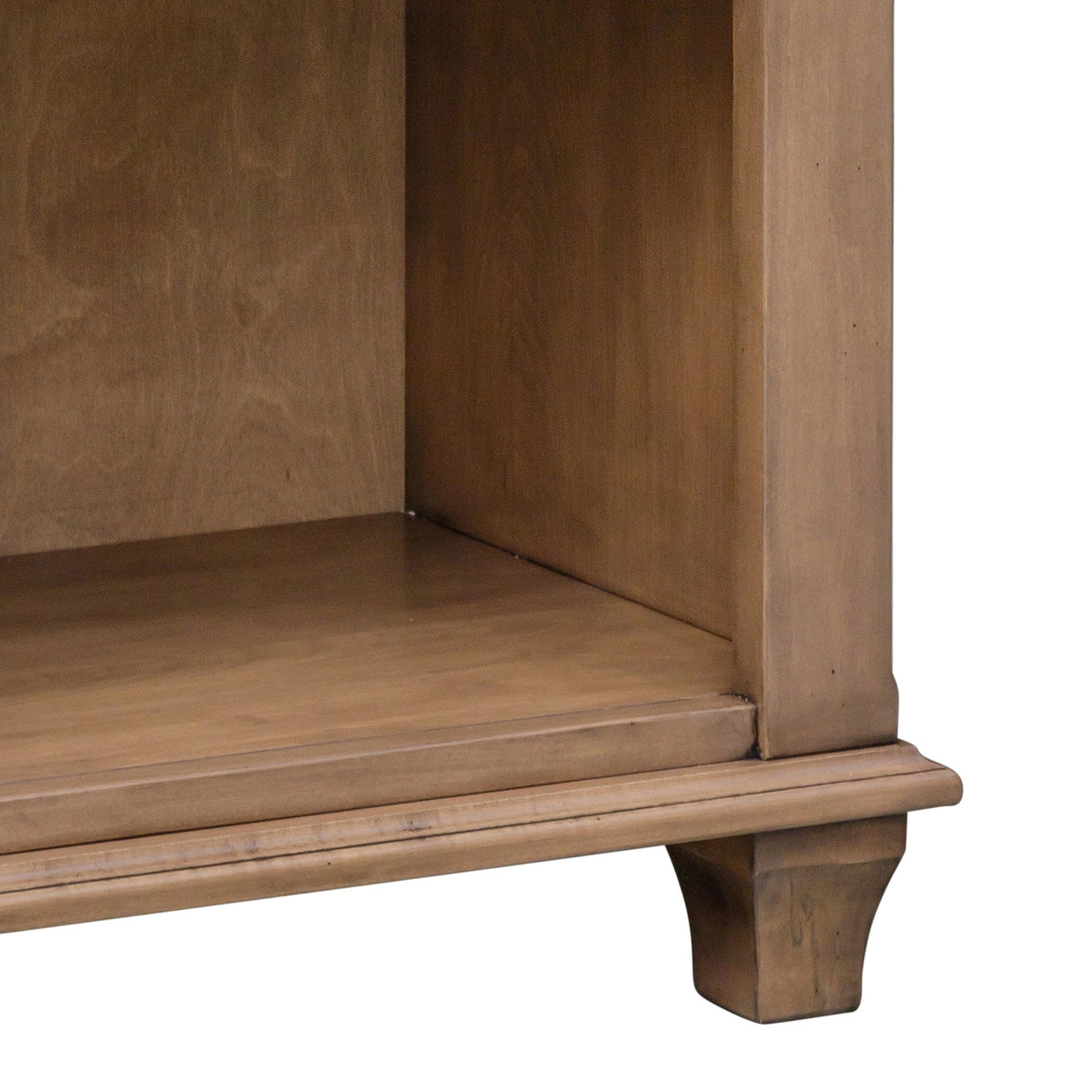 Detail of the open shelf compartment and shaped tapered foot on a light stained nightstand with molded base trim