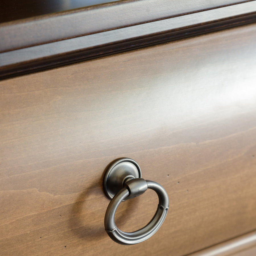Close-up of the antique pewter ring drawer pull on a light stained nightstand drawer front with a dark top edge