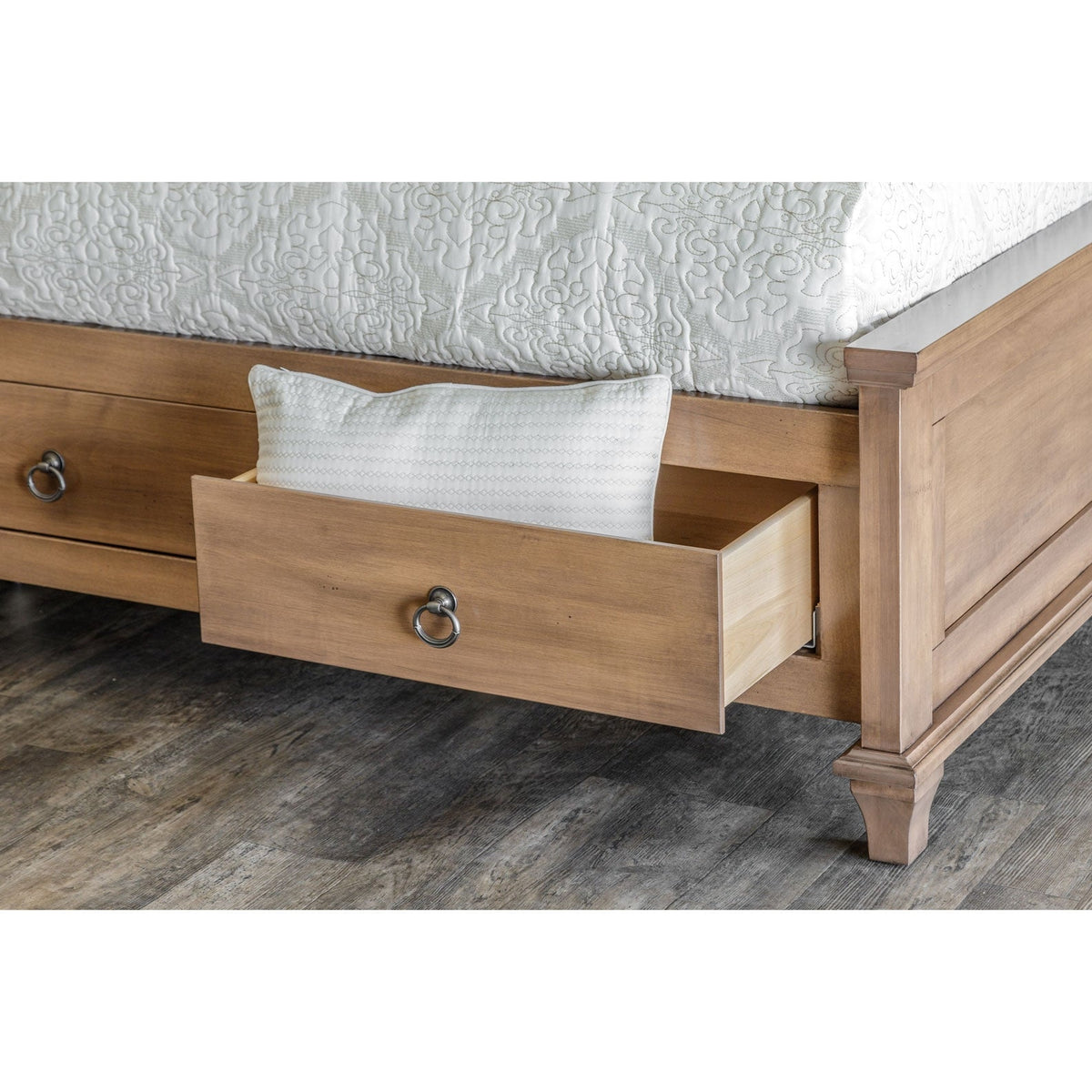 Under-bed captain drawer pulled open holding a pillow, beside the panel footboard on gray plank flooring