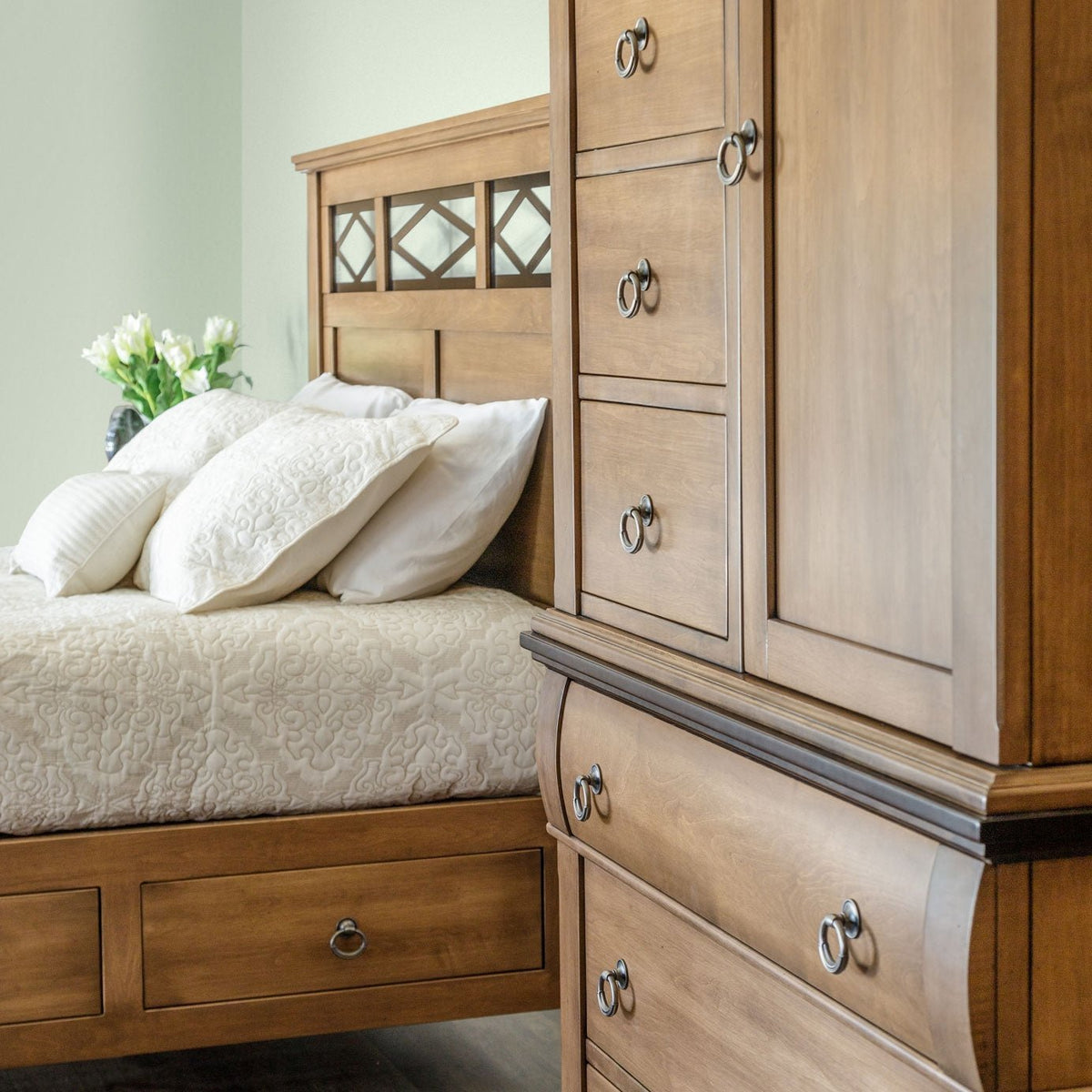 Tall door and drawer armoire beside a lattice headboard bed with white bedding in a soft green bedroom