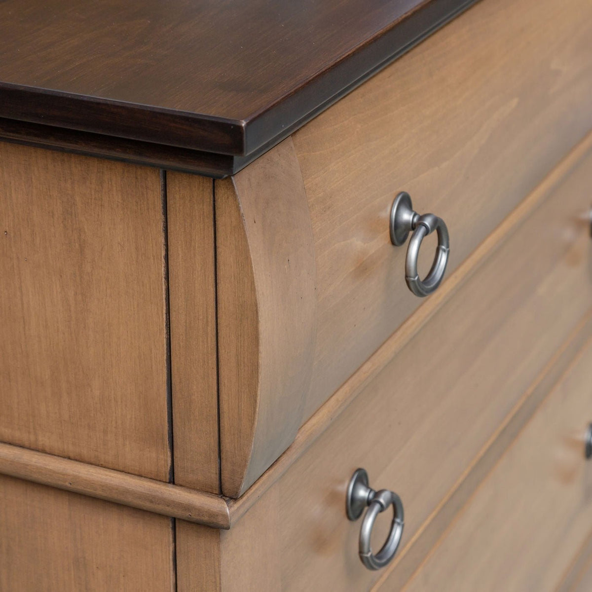 Corner detail showing the dark walnut top edge and bowed drawer front of a light almond drawer armoire