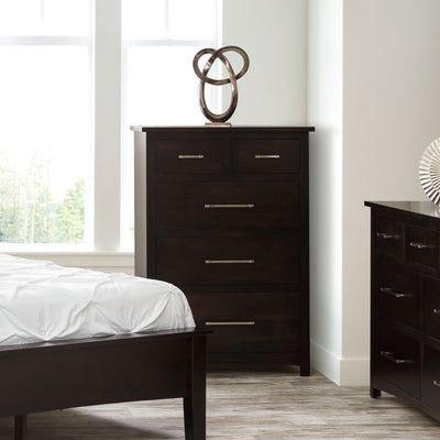 Espresso five drawer chest of drawers with silver bar pulls beside a bed and matching dresser by tall windows