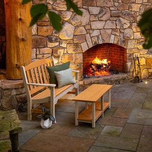 Natural teak poly garden bench with cushions beside a low shelf table at an outdoor stone fireplace